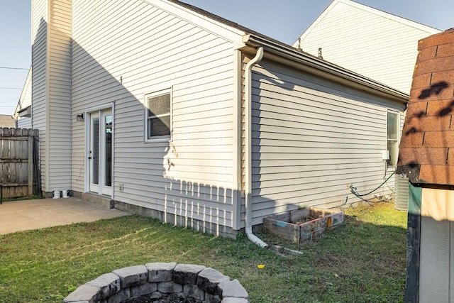 view of side of property with a fire pit, a lawn, a chimney, fence, and a patio area