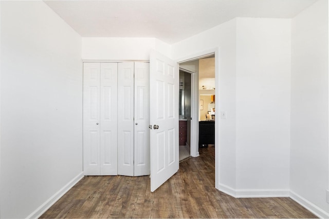 unfurnished bedroom featuring a closet, baseboards, and dark wood-type flooring