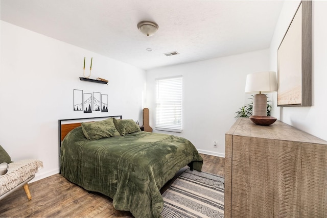 bedroom with wood finished floors, visible vents, and baseboards