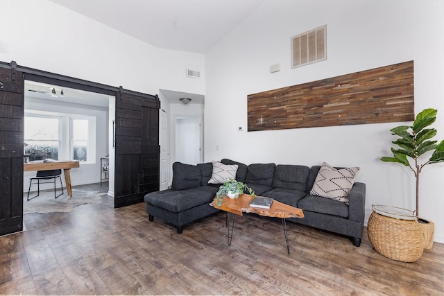 living area featuring high vaulted ceiling, wood finished floors, visible vents, and a barn door