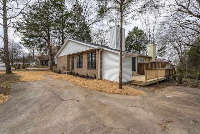 view of property exterior with a chimney, brick siding, and a deck