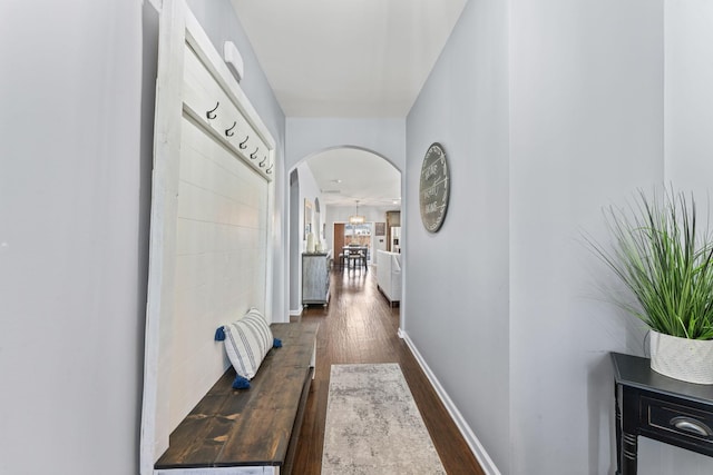 hallway featuring arched walkways, baseboards, and wood finished floors