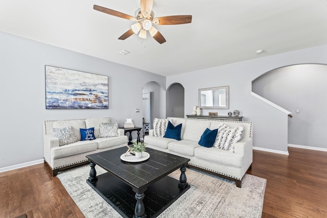 living area with arched walkways, wood finished floors, a ceiling fan, and baseboards