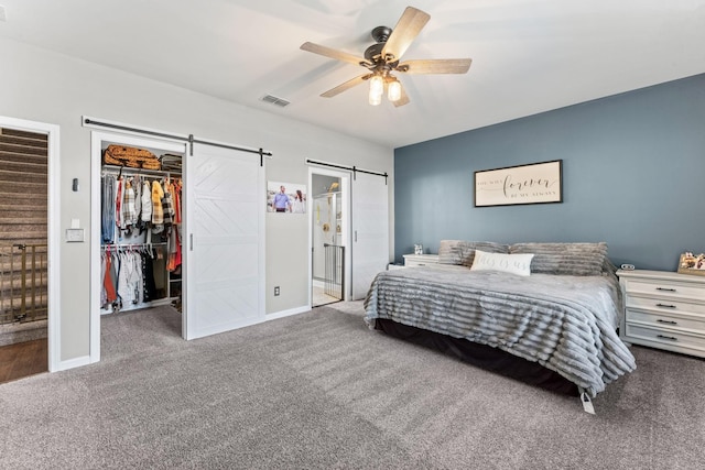 bedroom with a barn door, carpet flooring, visible vents, a ceiling fan, and a walk in closet