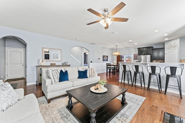 living room with a ceiling fan, arched walkways, baseboards, and wood finished floors