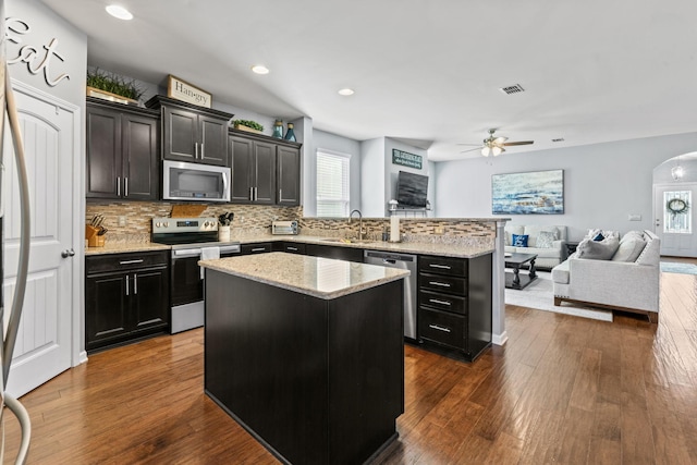 kitchen with stainless steel appliances, arched walkways, dark wood finished floors, and a kitchen island