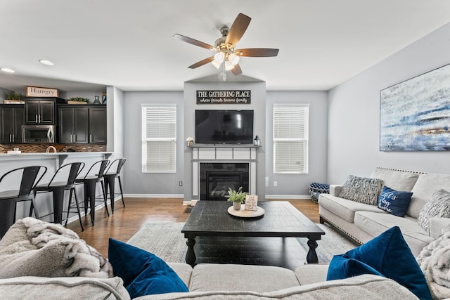 living area with a wealth of natural light, baseboards, wood finished floors, and a glass covered fireplace