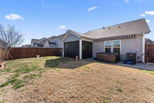 back of property featuring a yard, a hot tub, a sunroom, cooling unit, and a fenced backyard