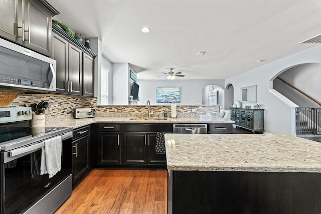 kitchen featuring tasteful backsplash, appliances with stainless steel finishes, wood finished floors, a peninsula, and a sink