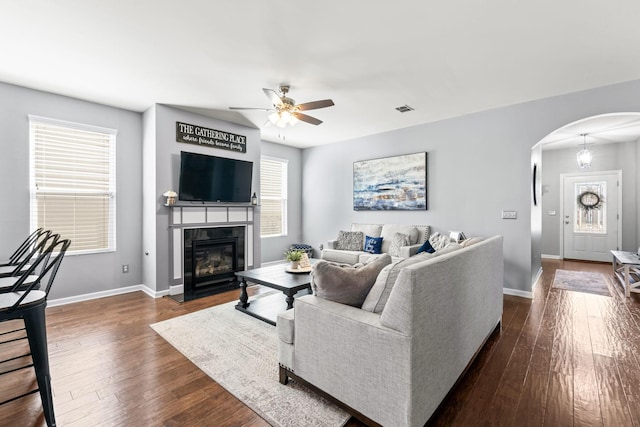 living room with arched walkways, a fireplace with flush hearth, dark wood finished floors, and baseboards