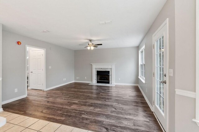 unfurnished living room featuring a high end fireplace, ceiling fan, baseboards, and wood finished floors