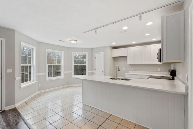 kitchen with light countertops, stainless steel microwave, white cabinetry, a sink, and range