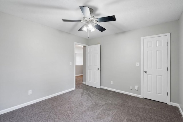 unfurnished bedroom featuring a ceiling fan, dark carpet, and baseboards