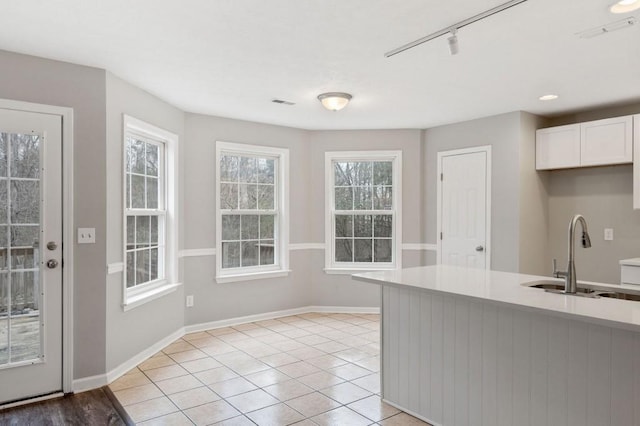 kitchen with light tile patterned flooring, a sink, baseboards, white cabinets, and light countertops