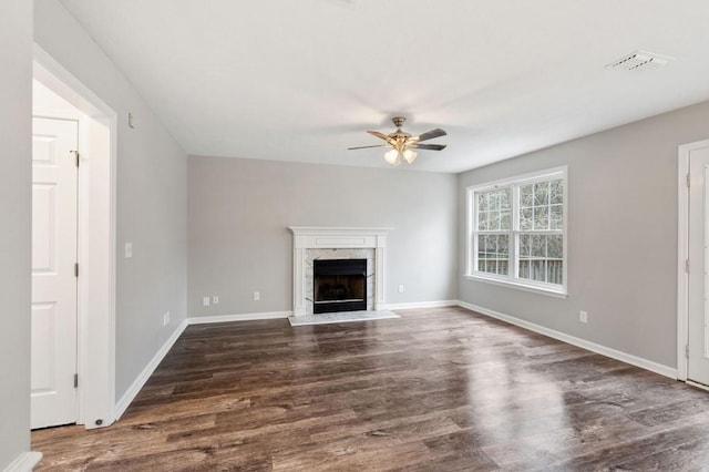 unfurnished living room with visible vents, a premium fireplace, dark wood-type flooring, ceiling fan, and baseboards