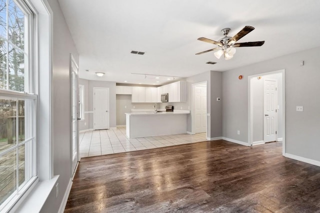 unfurnished living room featuring light wood-style floors, visible vents, baseboards, and a ceiling fan