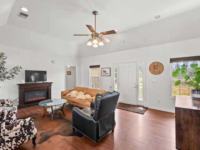 living area featuring visible vents, baseboards, vaulted ceiling, hardwood / wood-style floors, and a glass covered fireplace