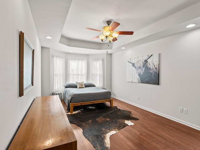 bedroom with baseboards, a raised ceiling, a ceiling fan, wood finished floors, and recessed lighting