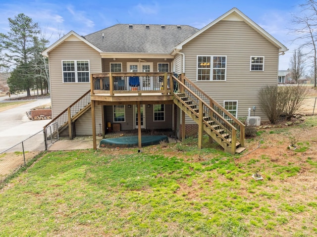 rear view of property with a shingled roof, a wooden deck, stairway, fence, and a yard