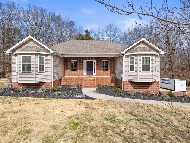 ranch-style house featuring a porch, a front yard, roof with shingles, and brick siding