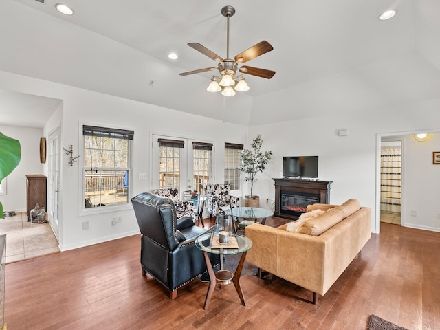 living room featuring baseboards, a glass covered fireplace, lofted ceiling, hardwood / wood-style floors, and recessed lighting