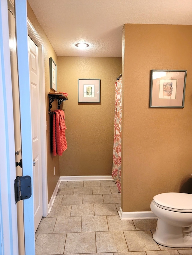 bathroom with toilet, a textured ceiling, and baseboards