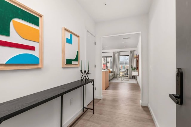 hallway featuring light wood finished floors, visible vents, and baseboards