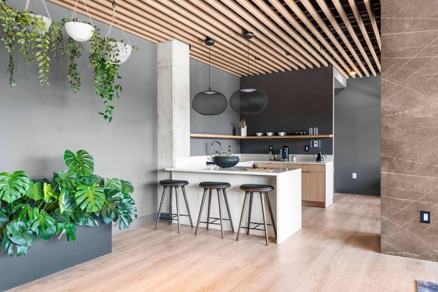 kitchen featuring light countertops, hanging light fixtures, light wood-style flooring, a peninsula, and a kitchen breakfast bar