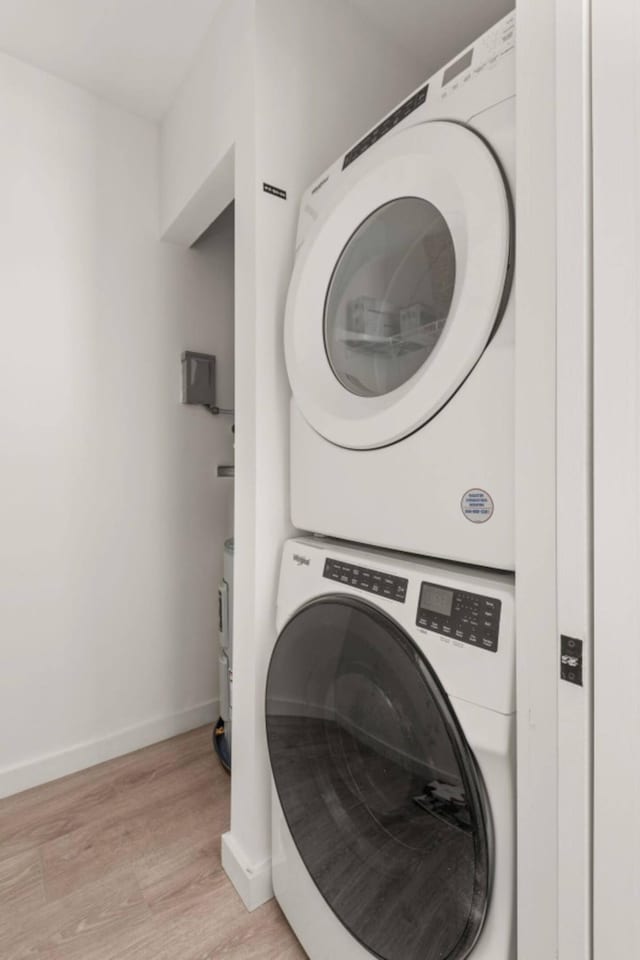 laundry room featuring laundry area, light wood-style floors, stacked washing maching and dryer, and baseboards