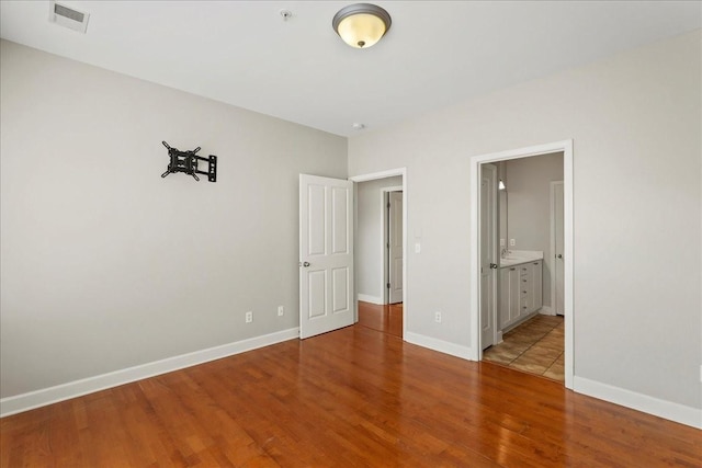 unfurnished bedroom featuring visible vents, baseboards, wood finished floors, and ensuite bathroom