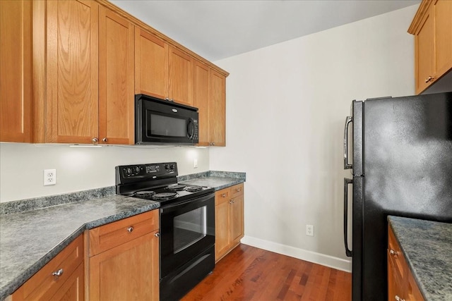 kitchen with brown cabinetry, dark wood-style floors, baseboards, black appliances, and dark countertops