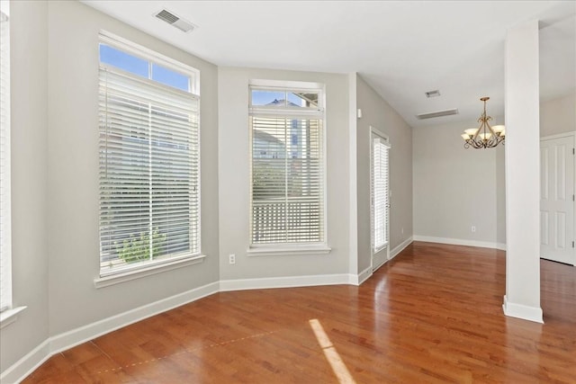 empty room featuring visible vents, baseboards, an inviting chandelier, and wood finished floors