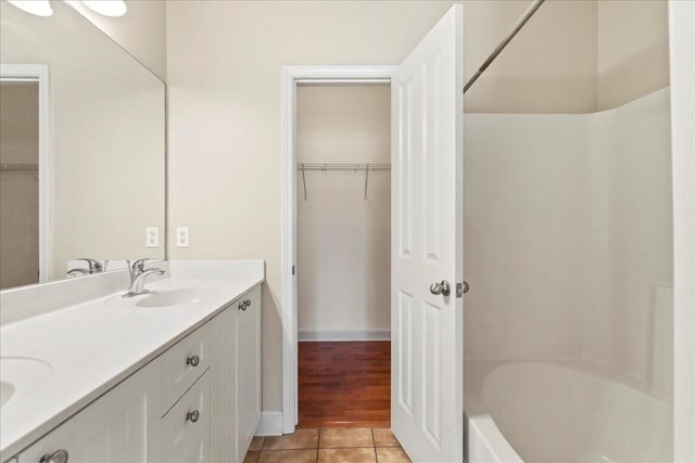 full bath with baseboards, double vanity, a sink, a walk in closet, and tile patterned floors