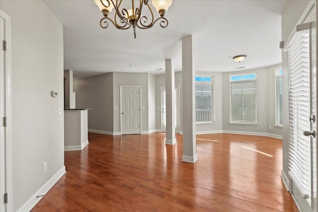 foyer entrance with baseboards, an inviting chandelier, wood finished floors, and ornate columns