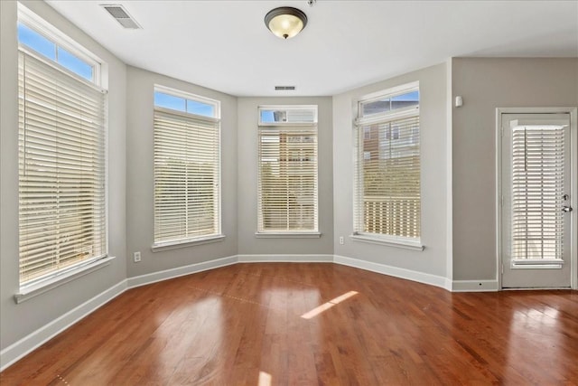 unfurnished dining area with visible vents, plenty of natural light, wood finished floors, and baseboards