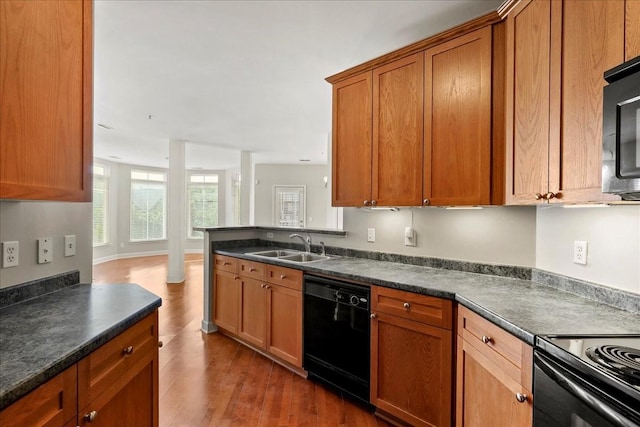 kitchen with dark countertops, dark wood finished floors, brown cabinets, black appliances, and a sink