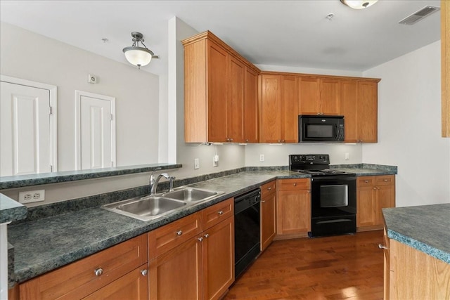 kitchen with visible vents, black appliances, a sink, dark countertops, and wood finished floors