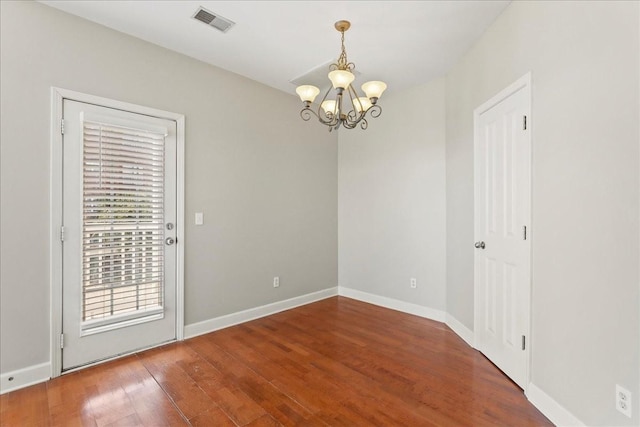 spare room featuring a chandelier, visible vents, baseboards, and wood finished floors