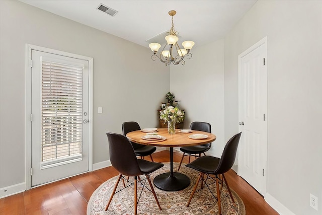 dining space with a notable chandelier, wood finished floors, visible vents, and baseboards