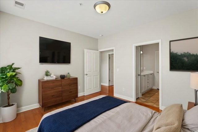 bedroom with visible vents, light wood-style flooring, ensuite bath, and baseboards