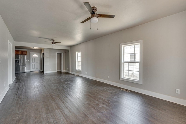 empty room with dark wood-type flooring, a healthy amount of sunlight, visible vents, and a ceiling fan