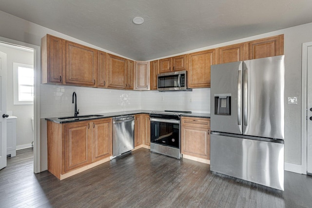 kitchen featuring stainless steel appliances, dark countertops, a sink, and dark wood-style floors