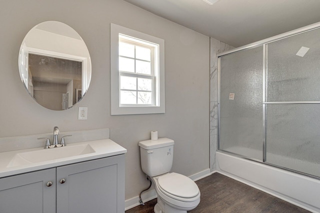 full bathroom featuring bath / shower combo with glass door, toilet, vanity, wood finished floors, and baseboards