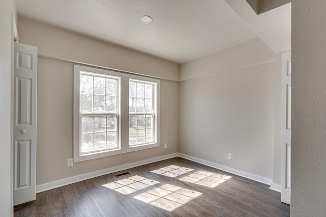 unfurnished room with dark wood-style flooring, visible vents, and baseboards