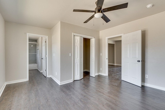 unfurnished bedroom featuring baseboards, a ceiling fan, connected bathroom, dark wood-type flooring, and a closet