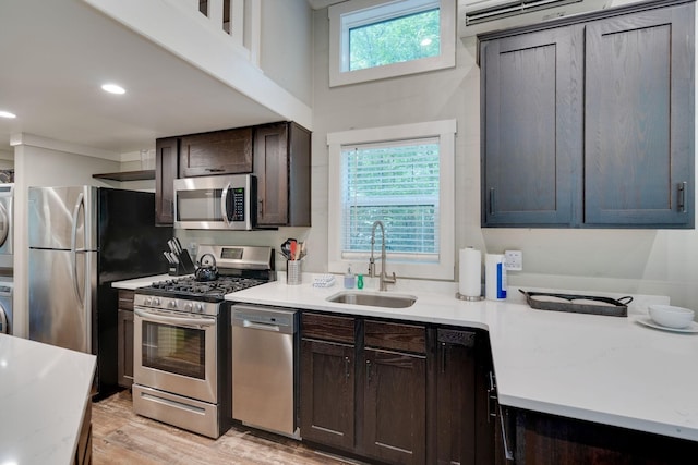 kitchen featuring stacked washer and dryer, light wood-style flooring, appliances with stainless steel finishes, dark brown cabinets, and a sink