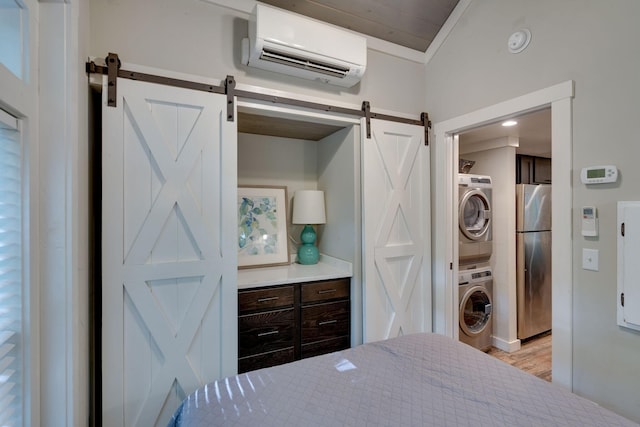 bedroom with a barn door, stacked washer / drying machine, freestanding refrigerator, vaulted ceiling, and an AC wall unit