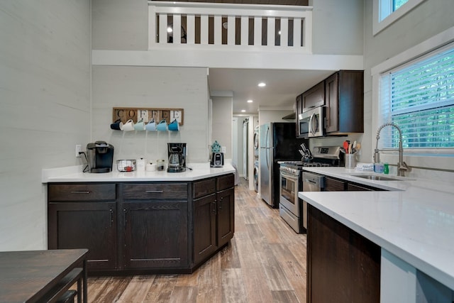 kitchen featuring a high ceiling, stainless steel appliances, dark brown cabinets, light wood-style floors, and a sink