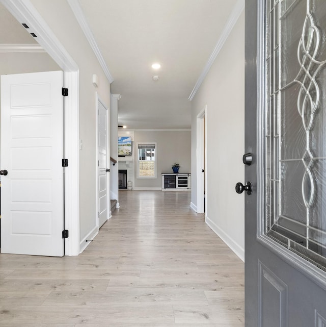 entryway with ornamental molding, light wood-style floors, and a fireplace