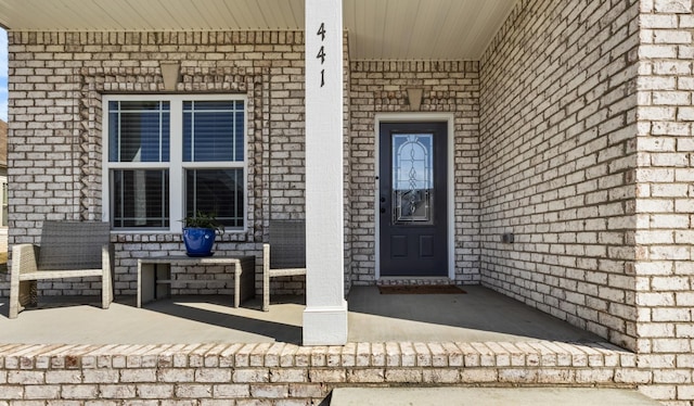 entrance to property featuring a porch and brick siding